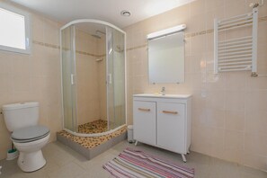 A bathroom with a toilet, a shower enclosure, a sink with a mirror, and a towel rack.