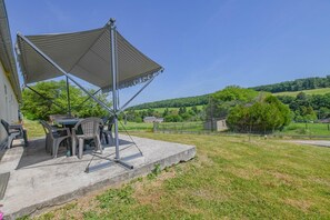 An outdoor patio with a table and chairs, a pergola, and a view of a green landscape.