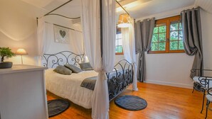A four-poster bed with white curtains, a bedside lamp, and a potted plant.