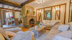 A cozy living room with a stone fireplace, wooden beams, and a chandelier.