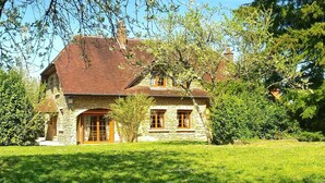 A stone house with a pitched roof, a central entrance with a door and windows, and a well-maintained lawn.