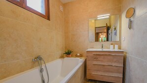A bathroom with a bathtub, a wooden vanity with a mirror, and a small plant.
