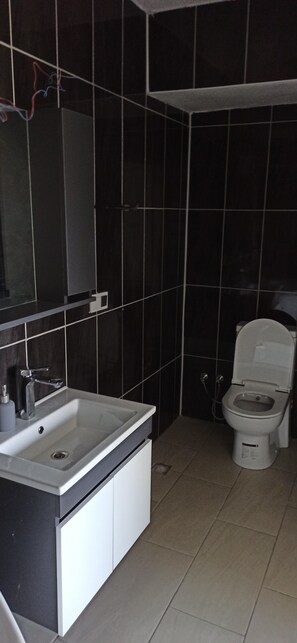 A modern bathroom with a white sink, dark tiles, and a toilet.
