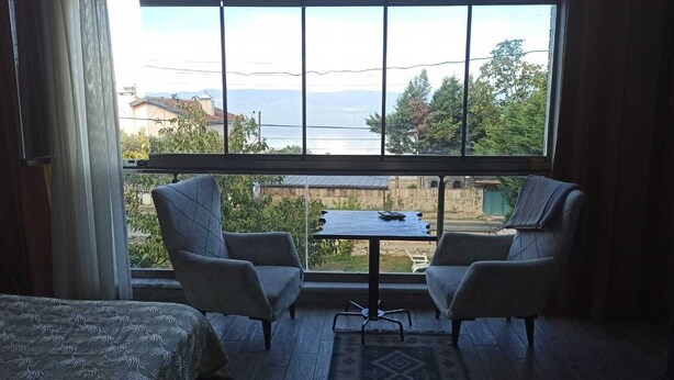 Une pièce avec deux fauteuils placés face à une petite table, une vue sur un plan d’eau et des montagnes, et une couvre-lit à motifs.
