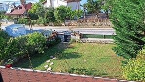 Un jardin arrière d’une maison, avec une pelouse, un petit espace aménagé en jardin et un mur en pierre.
