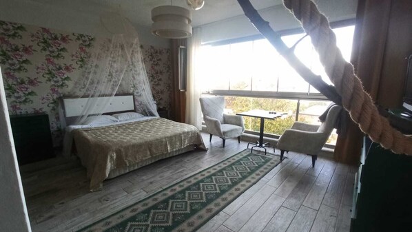 A bedroom with a bed, two chairs, a small table, and a window with curtains.