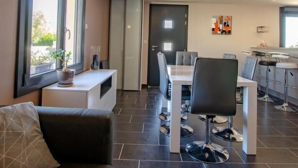 A modern living room with a sofa, dining table, and chairs. There is a staircase leading to an upper level. - Chez Mimi - Plessis Barbuise (PLESSIS BARBUISE)