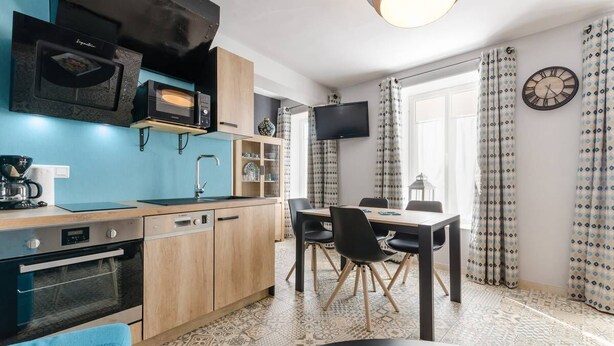 Una cocina compacta con electrodomésticos modernos, un comedor con mesa y sillas, y un televisor montado en la pared.