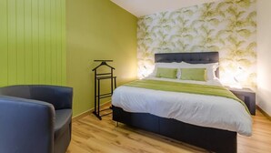Un dormitorio con una cama, una silla, una mesita de noche y una pared con un diseño de hojas.