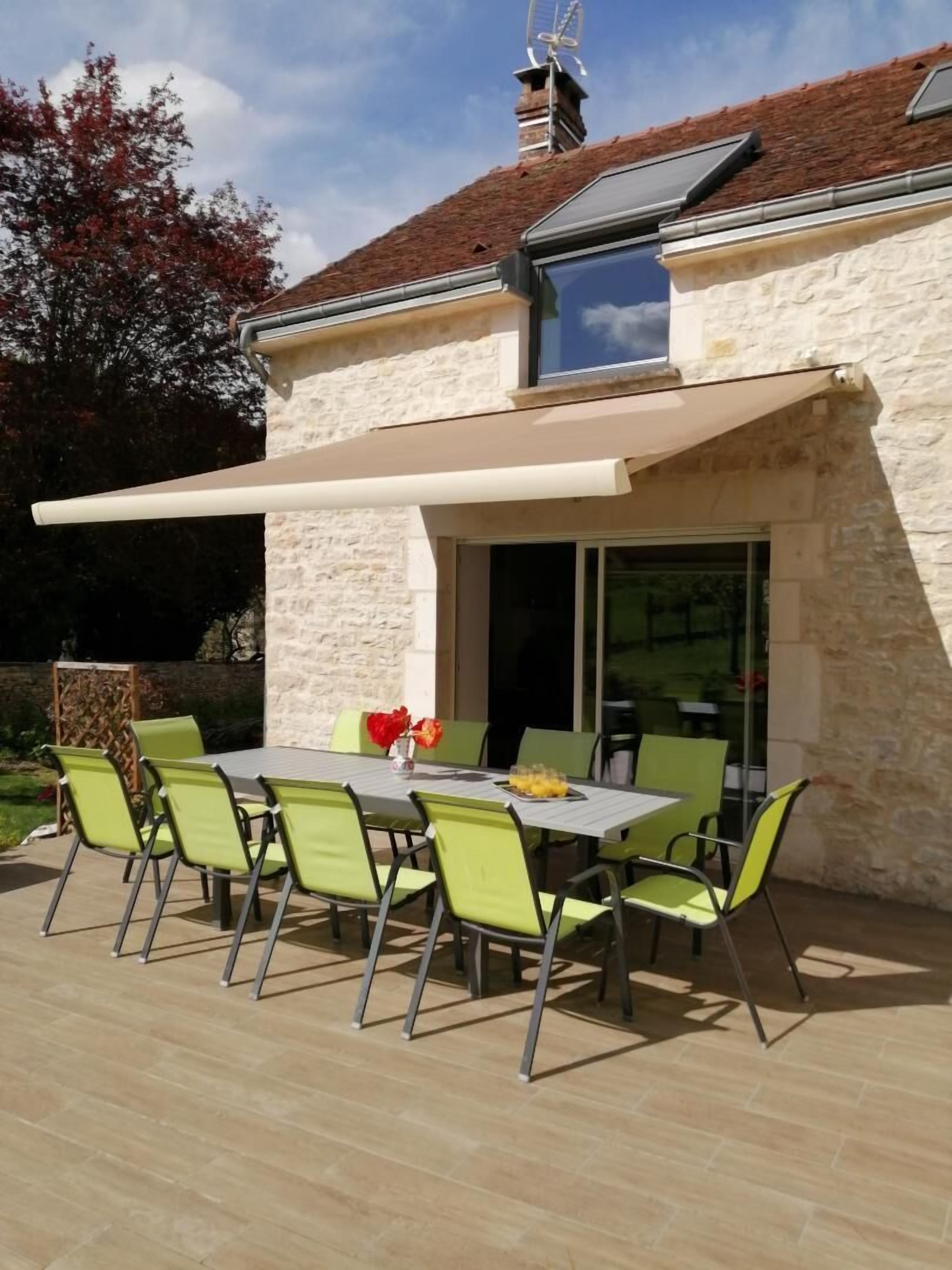 Une terrasse avec une table et des chaises, un espace abrité et un bâtiment en pierre doté d’une cheminée.
