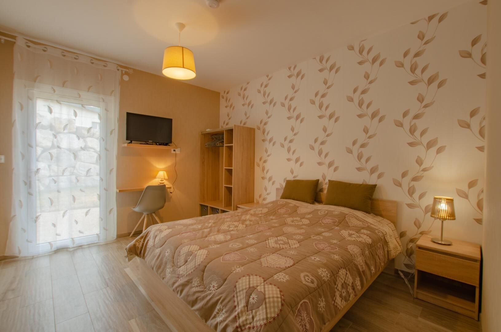 Un dormitorio con cama, escritorio, silla, armario y televisor montado en la pared.