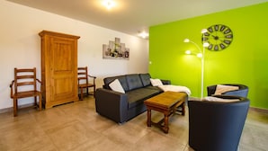 Una sala de estar con un sofá, dos sillones, un aparador de madera, una mesa de centro y una pared verde con un reloj.