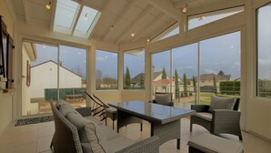 A spacious patio with a dining table and wicker furniture, large windows offering views of the surrounding area.