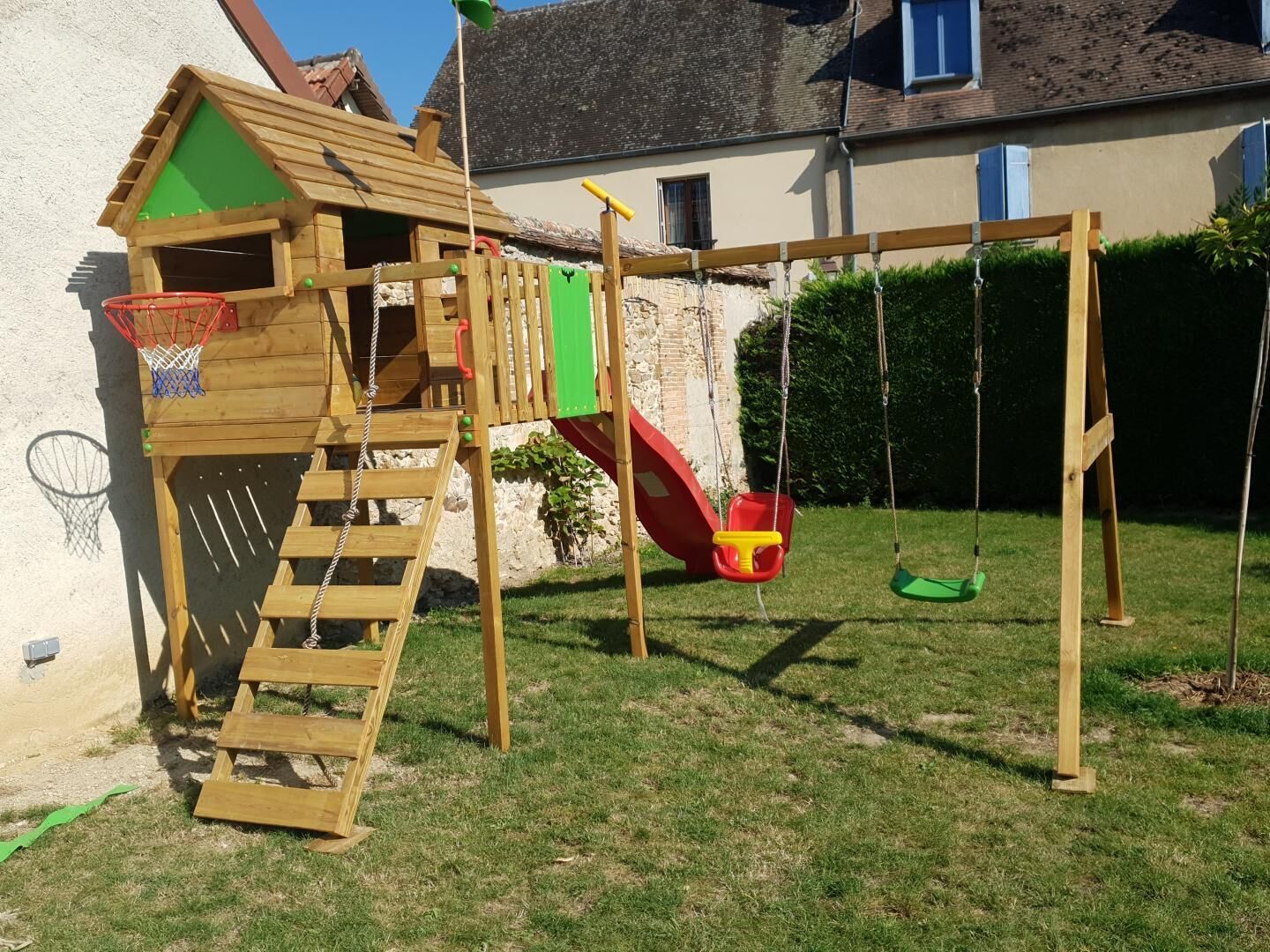 A wooden playhouse with a basketball hoop and a slide.