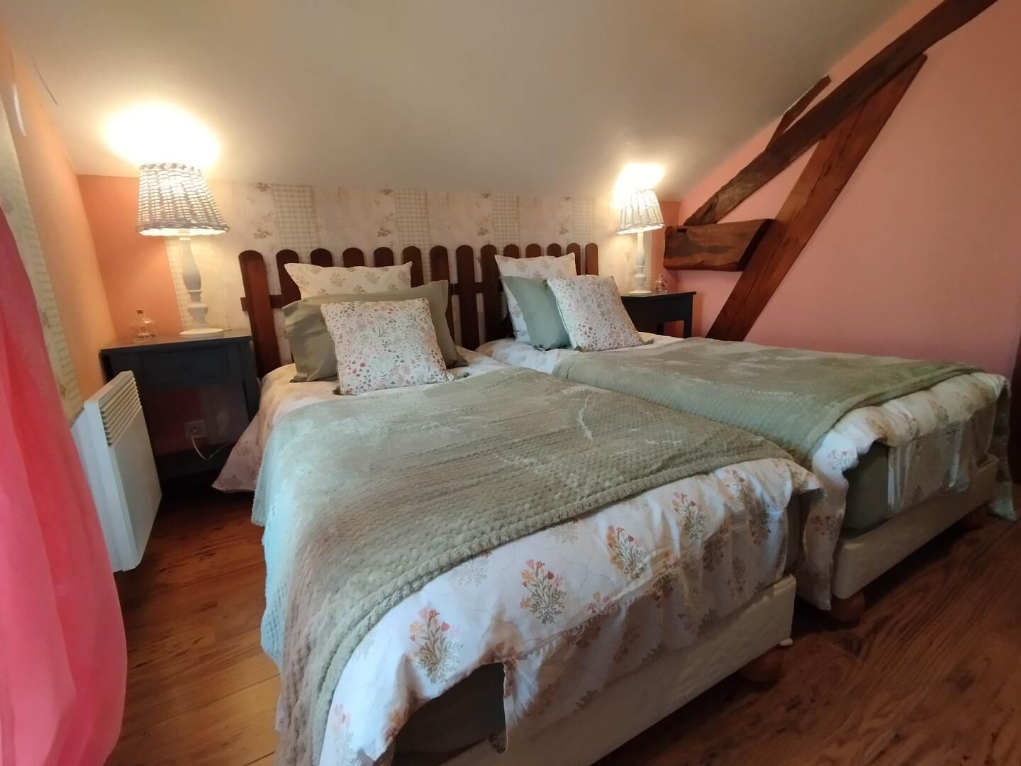 A bedroom with two beds, wooden headboard, bedside lamps, floral bedding, and a sloped ceiling.