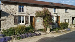 A stone building with a tiled roof, a wooden door, and a small porch with a flower box. - La Clémenceraie - Baroville (BAROVILLE)