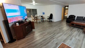 A living room with a flat-screen TV, wooden flooring, a sofa, a coffee table, and a dining area with chairs and a table. - Penguin Cabin The Utmost Family Mt Rainier Getaway (Ashford)