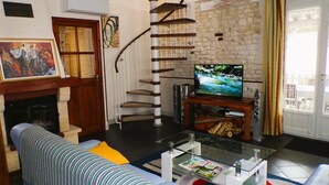 A living room with a sofa, a fireplace, a television, and a staircase. - La Salle de Danse - Eaux Puiseaux (EAUX PUISEAUX)