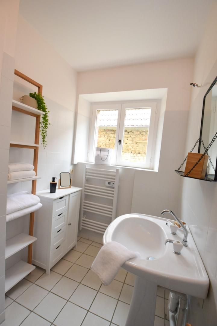 A modern bathroom with a white sink, a mirror, and a window.