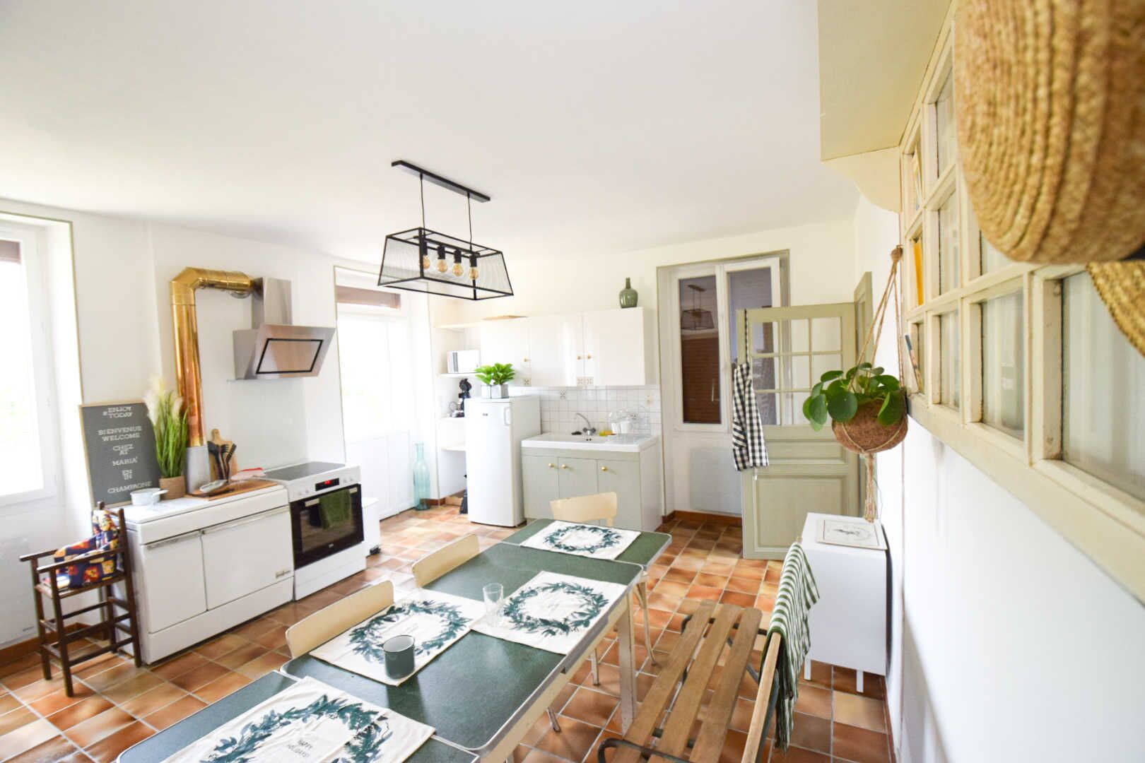 A modern kitchen with a dining area, white cabinets, a built-in oven, and a hanging plant.