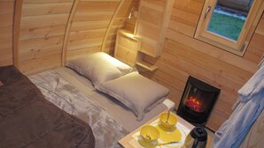 Ein gemütliches Blockhauszimmer mit einem Bett, einem kleinen Tisch mit Wasserkocher und einem Kamin.