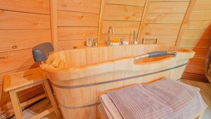 Eine Holzsauna mit einer großen Badewanne, einer hölzernen Sitzbank und einem Handtuch auf einem Ständer.