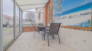 Un patio techado con mesa y sillas, un mural con motivo de playa y vistas del entorno.