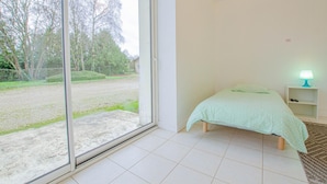 Un dormitorio con una cama, una mesita de noche y una lámpara. Hay una puerta corrediza de vidrio que da a una zona cubierta de césped.
