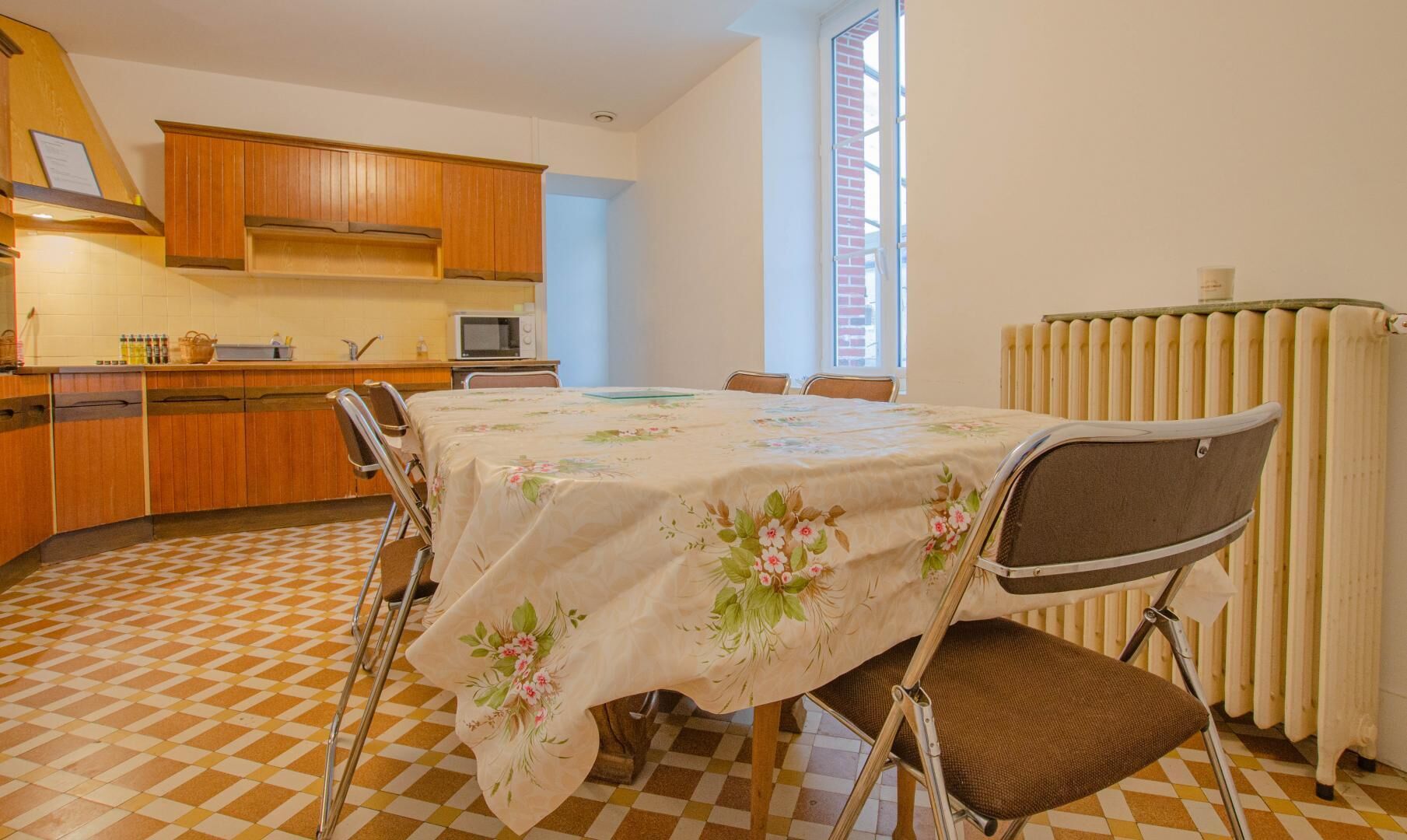 Une cuisine compacte avec des meubles en bois, un four à micro-ondes et un coin repas comprenant une table recouverte d’une nappe à motifs floraux.