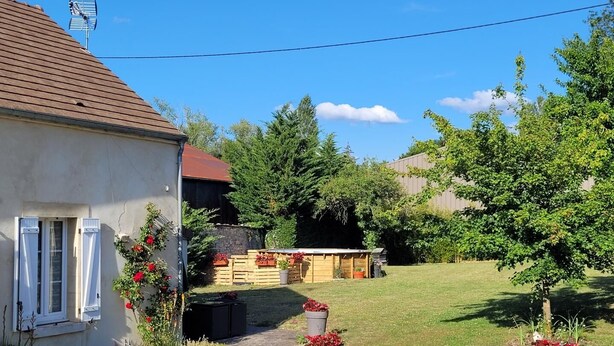 A house with a red roof, a garden with red flowers, and a wooden structure in the yard.
