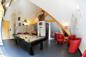 Une table de billard dans une pièce avec des chaises rouges et un espace mezzanine avec des poutres en bois.