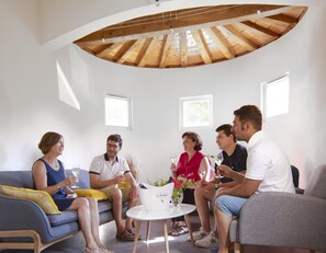 Un groupe de personnes est assis sur un canapé dans une pièce dont le plafond est en bois et qui possède de petites fenêtres.