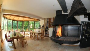 A cozy room with a fireplace, wooden furniture, and large windows offering a view of the outdoors. - La Halte Saint Bernard (BAR SUR SEINE)