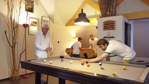 A pool table in a room with a lofted ceiling, wooden beams, and a hanging light fixture. - La Halte Saint Bernard (BAR SUR SEINE)