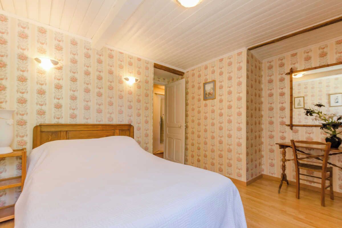 A bedroom with a wooden bed, floral wallpaper, a wooden chair, and a mirror.