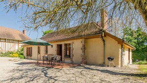 Une maison avec une allée en gravier, une terrasse avec une table et des chaises, et un barbecue.