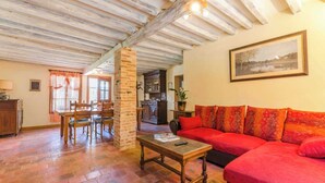 Un salon chaleureux avec un canapé rouge, une table basse en bois et un coin repas agrémenté d’un pilier en briques.
