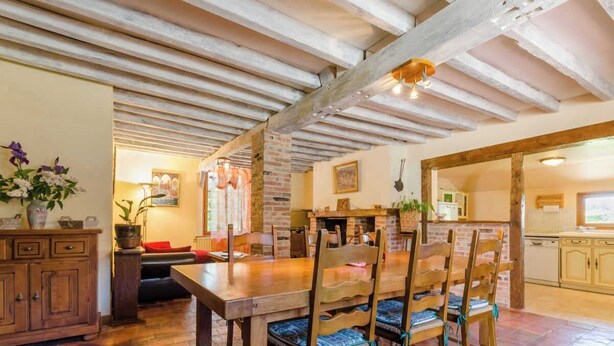 Un coin repas avec une table et des chaises en bois, une cheminée en briques et des poutres apparentes au plafond.