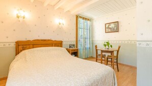 Une chambre à coucher avec un grand lit, une tête de lit en bois, une petite table avec des chaises, une fenêtre avec des rideaux et un tableau accroché au mur.