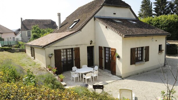 A two-story house with a sloped roof, a patio with outdoor furniture, and a garden area. - House (BLIGNY)