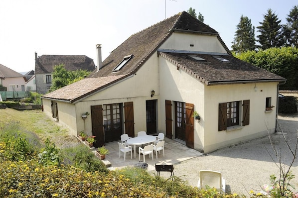 A two-story house with a sloped roof, a patio with outdoor furniture, and a garden area.