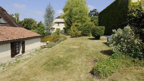 A grassy courtyard with a building on the left, a tree in the center, and a hedge on the right. - House (BLIGNY)