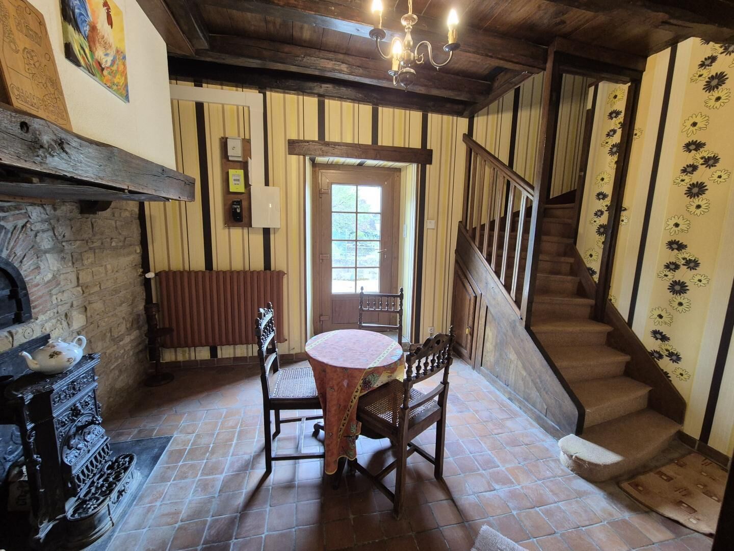 A room with a fireplace, a round table with chairs, a wooden bench, a staircase, and a door with a window.
