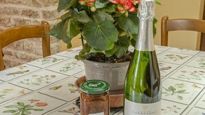 A table with a floral tablecloth, a bottle of champagne, a potted plant, and a jar of jam. - House (BLIGNY)