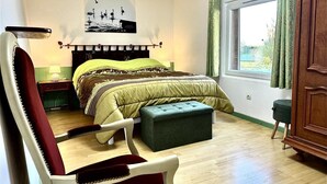 Un dormitorio con cama, una silla, una ventana y un cuadro en la pared.