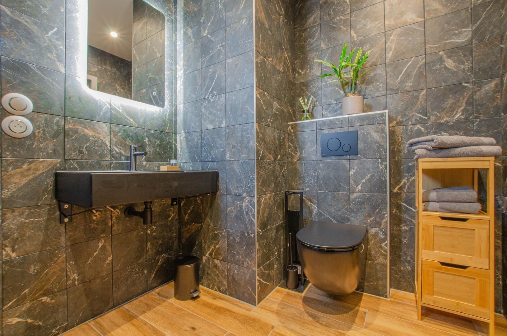 Un baño moderno con detalles de mármol, un lavabo con espejo, inodoro y repisa con toallas.