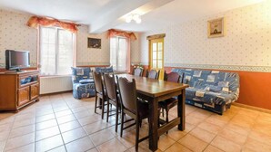 Un comedor con mesa y sillas de madera, un sofá y una televisión sobre un mueble.