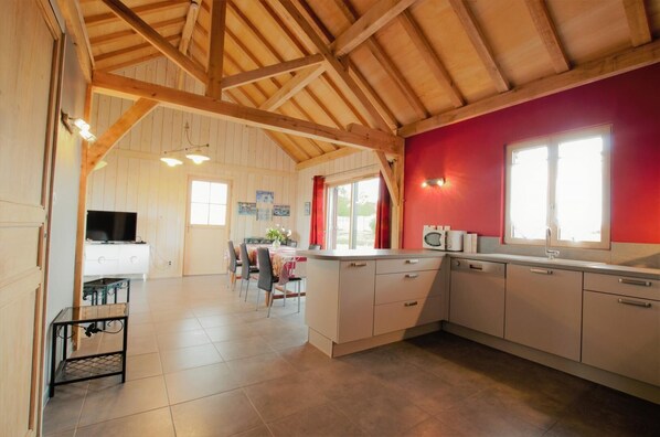 Une cuisine spacieuse avec des poutres apparentes, un coin repas avec une table et des chaises, et un mur d’accent de couleur rouge.