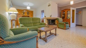 Ein geräumiges Wohnzimmer mit einem grün gemusterten Sofa, einem Holztisch und einem Kamin.