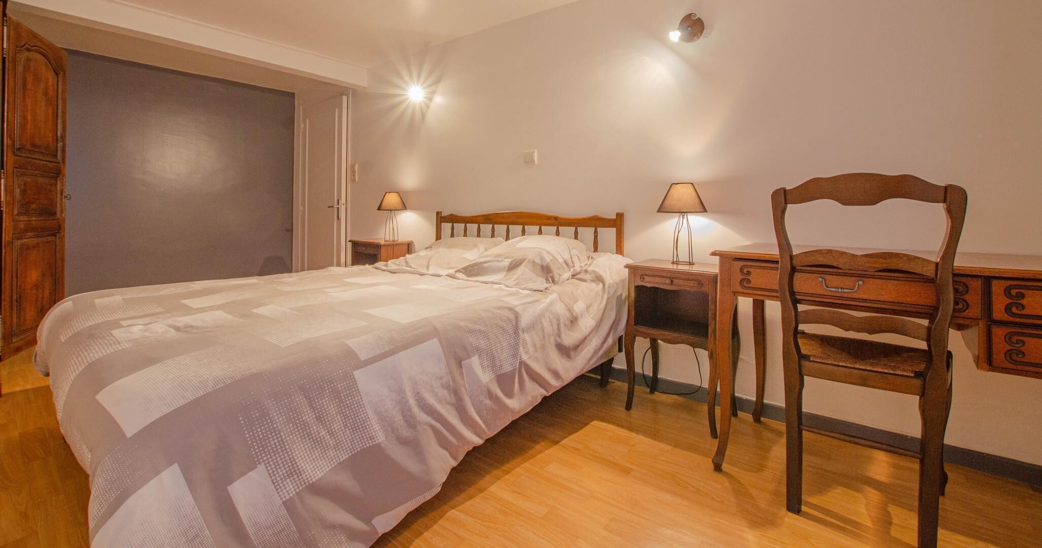 A bedroom with a bed, a wooden chair, a desk, and two lamps.